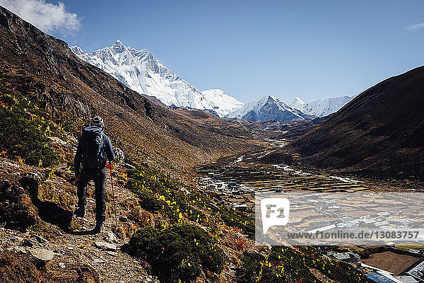 Rückansicht eines Wanderers mit Rucksack beim Bergwandern vor klarem blauen Himmel
