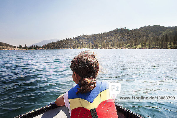 Rear view of girl wearing life jacket sitting in boat on lake