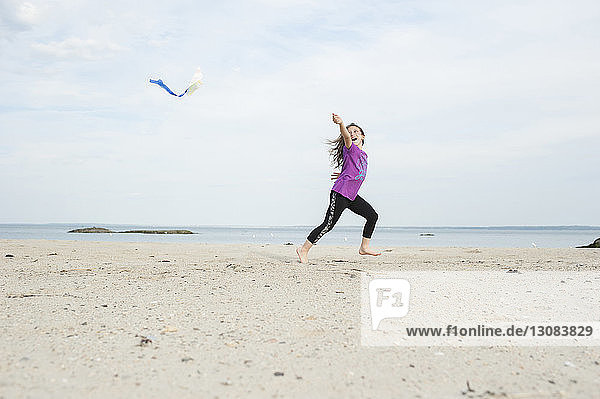 Girl playing with kite at beach against sky