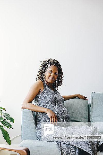 Porträt einer schwangeren Frau  die zu Hause auf einem Sofa an der Wand sitzt