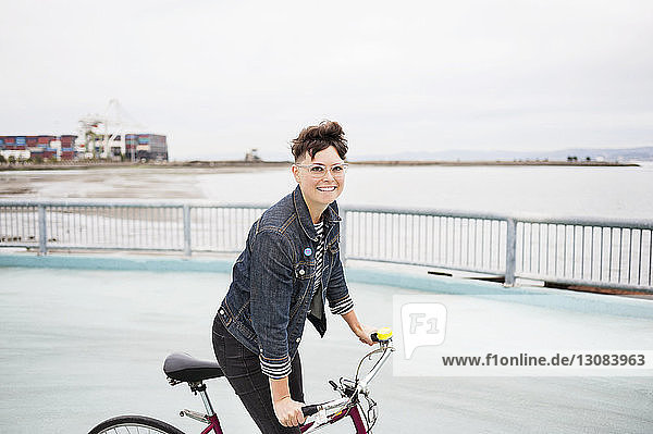 Portrait of happy woman riding bicycle on footpath by sea