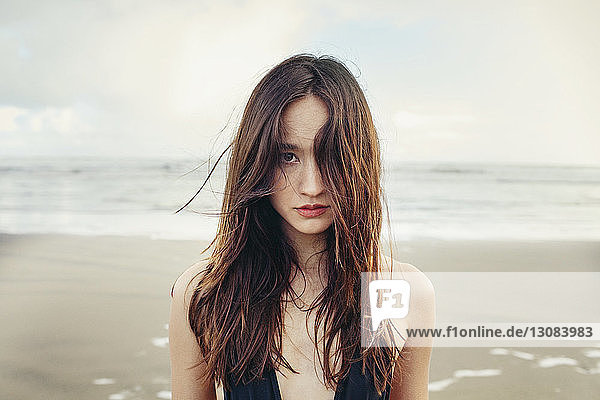 Portrait of beautiful woman standing at Bethells Beach against sea