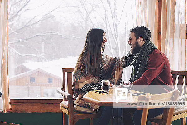 Happy couple looking at each other while sitting by window in cafe
