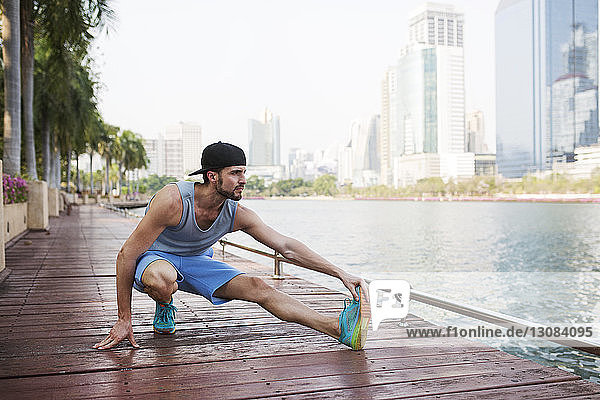 Man stretching on walkway by river against buildings