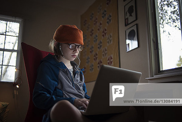 Junge benutzt Laptop-Computer  während er zu Hause auf einem Stuhl am Tisch sitzt