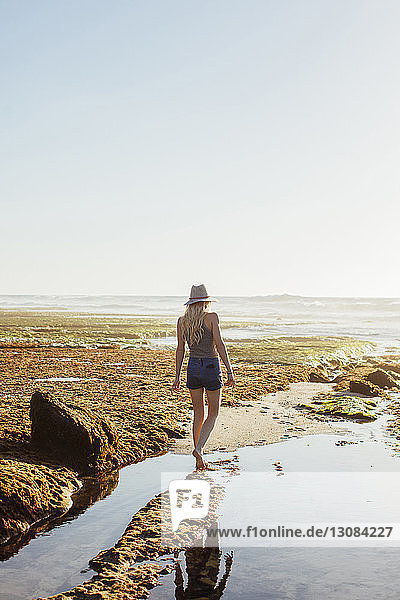 Rückansicht einer Frau  die am Strand bei klarem Himmel an einem sonnigen Tag am Strand spazieren geht