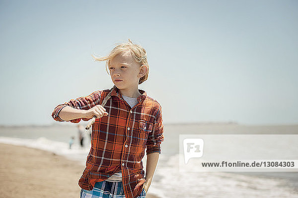 Thoughtful boy holding stick while walking on beach
