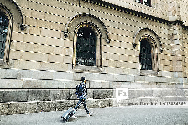 Seitenansicht eines Geschäftsmannes mit Gepäck  der auf einem Fußweg gegen ein Gebäude läuft