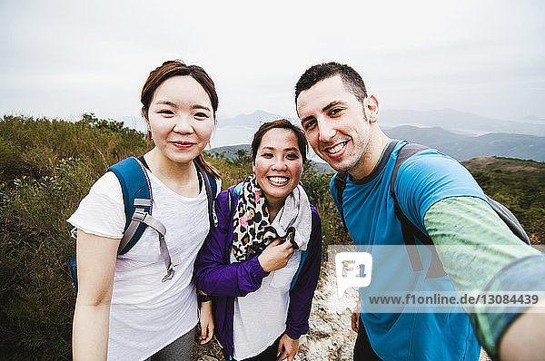 Portrait of happy friends standing on mountain against sky