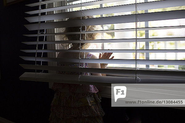 Girl looking through window while standing at home