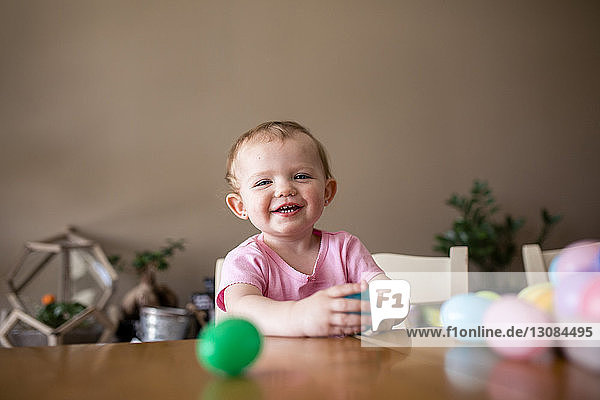 Porträt eines lächelnden Mädchens beim Spielen mit bunten Ostereiern auf dem heimischen Tisch