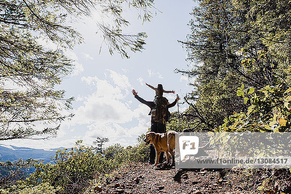 Männlicher Wanderer  der seine Tochter trägt  während er neben Hunden auf Berg gegen Himmel steht
