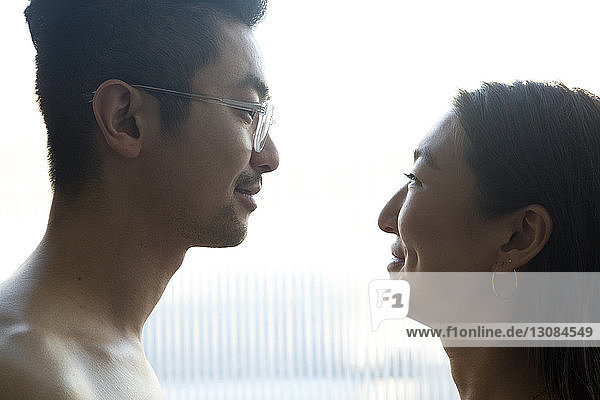 Seitenansicht eines glücklichen Paares  das sich gegenseitig ansieht  während es zu Hause am Fenster steht