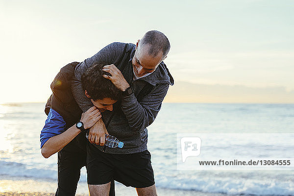 Father and son playing while exercising at beach against sky