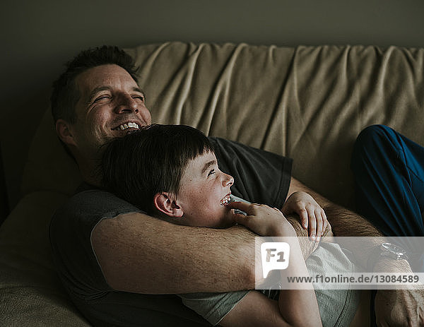 Happy father embracing son while lying on sofa at home