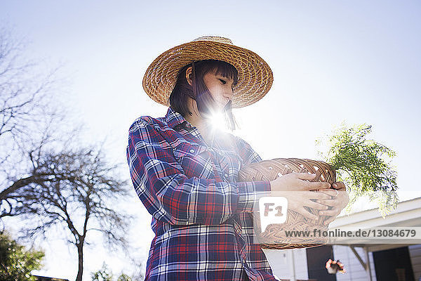 Junge Bäuerin trägt Korb bei sonnigem Wetter im Betrieb