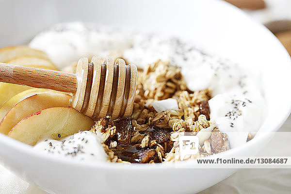 Nahaufnahme von Honiglöffel mit Apfelscheiben und Joghurt in Frühstückszerealien auf dem Tisch
