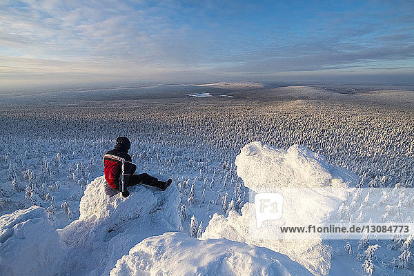 Wanderer betrachtet Aussicht  während er im schneebedeckten Berg gegen den Himmel sitzt
