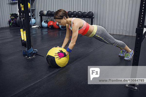 Athletin in voller Länge stützt sich im Fitnessstudio auf Medizinball