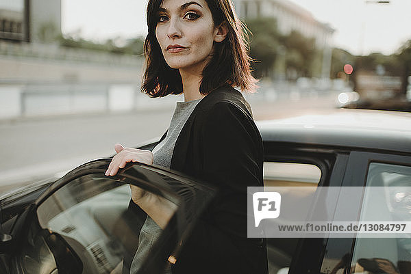Portrait of confident woman boarding into car in city