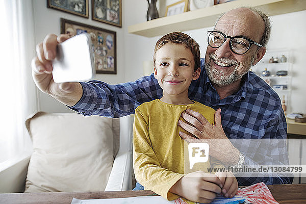Happy senior man taking selfie with grandson at home