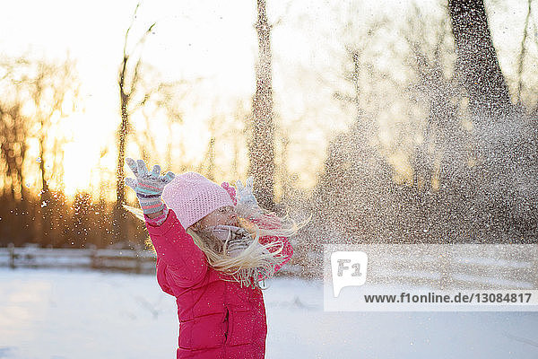 Girl in warm clothing throwing snow while standing against sky