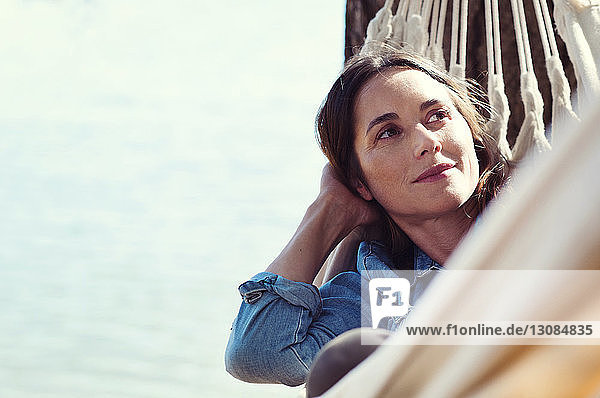 Thoughtful woman looking away while relaxing on hammock