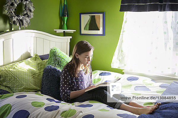 Mädchen liest Buch  während sie zu Hause auf dem Bett sitzt