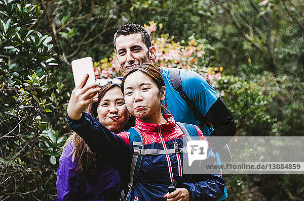 Fröhliche Freunde  die im Wald stehen und Selfie nehmen