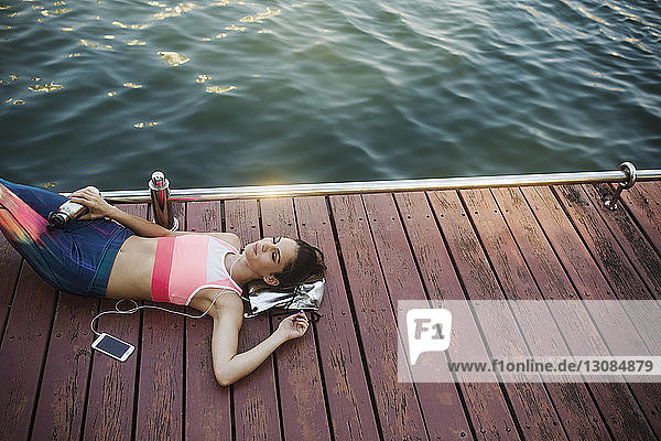High angle view of woman listening music and relaxing on wooden walkway