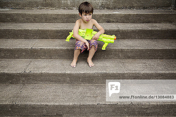 Boy sitting with water gun on stairs