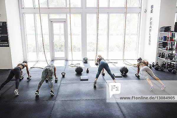 High angle view of athletes doing push-ups using dumbbells in crossfit gym