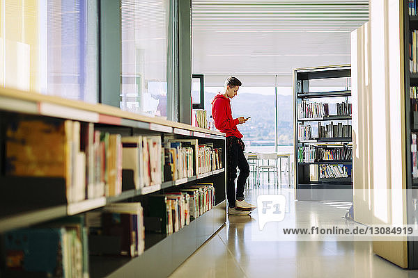 Seitenansicht eines Mannes  der ein Mobiltelefon benutzt  während er in der Bibliothek steht