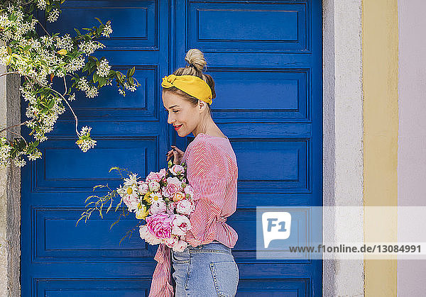 Seitenansicht einer Frau  die weg schaut  während sie den Blumenstrauss gegen die Tür hält