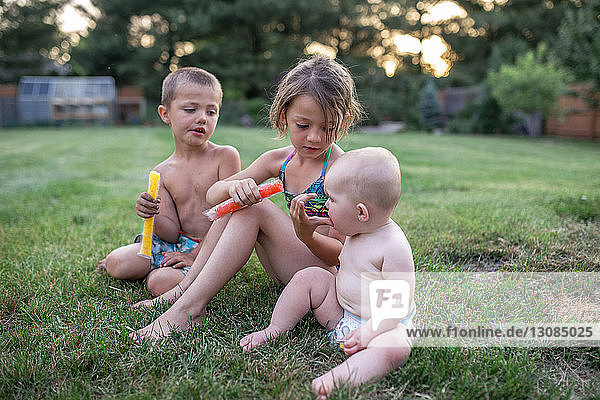 Mädchen füttert Schwester mit eisgekühlten Süßigkeiten  während sie beim Bruder im Hof sitzt