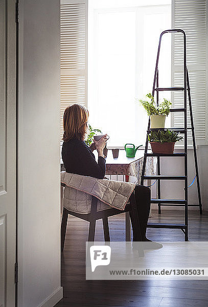 Frau trinkt Kaffee  während sie zu Hause auf einem Stuhl sitzt