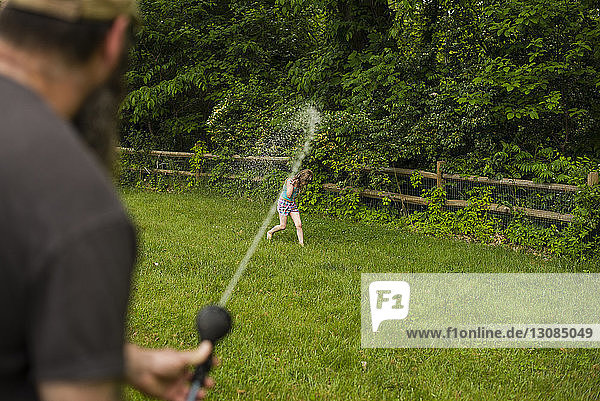 Playful father spraying water with hose on girl at backyard