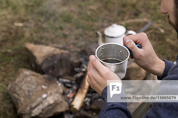 Ausgeschnittenes Bild eines Mannes  der am Lagerfeuer auf dem Campingplatz einen Teebecher hält