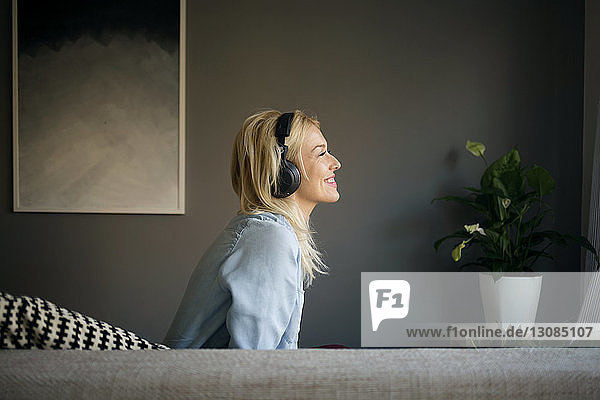 Seitenansicht einer glücklichen Frau  die Musik hört  während sie zu Hause auf dem Sofa sitzt