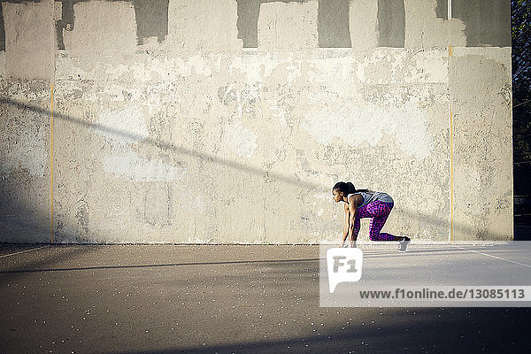 Frau in Startposition auf der Straße bereit  an der Mauer entlang zu laufen