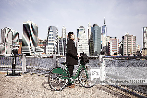 Seitenansicht eines Geschäftsmannes mit Fahrrad  der vom Aussichtspunkt aus die Stadt genießt