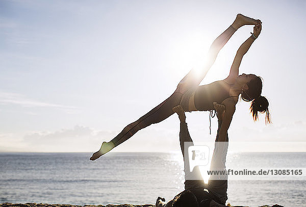 Mann hebt Frau beim Yoga am Strand gegen den Himmel