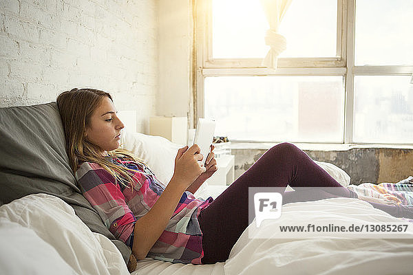 Seitenansicht eines Mädchens  das einen Tablet-Computer benutzt  während es auf dem Bett sitzt
