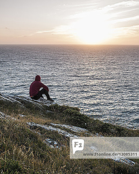 Seitenansicht eines Mannes  der bei Sonnenuntergang am Strand gegen den Himmel sitzt