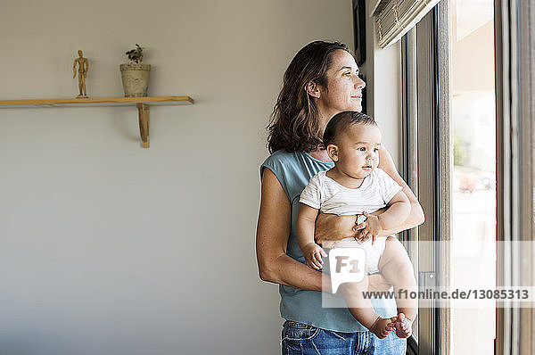 Mother with baby boy standing by window at home