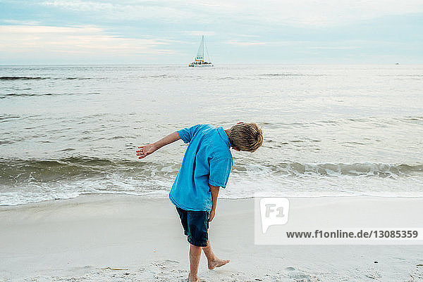 Rückansicht eines verspielten Jungen  der sich am Strand von Panama City gegen den Himmel beugt
