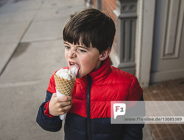 Boy looking away while licking ice cream on footpath in city