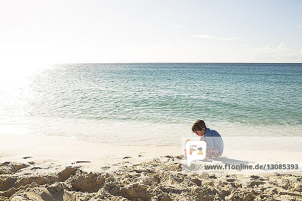 Junge spielt mit Sand am Strand gegen den Himmel an einem sonnigen Tag