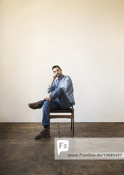 Porträt eines selbstbewussten Geschäftsmannes auf einem Stuhl  der im Büro an einer weißen Wand sitzt