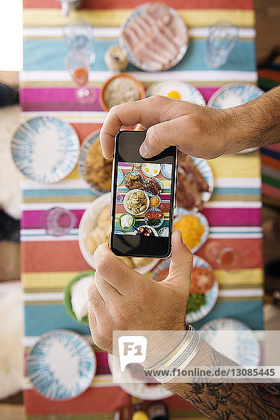 Cropped image of man's hands photographing food at table